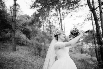 Blonde bride with wedding bouquet and bright make up at autumn pine wood. Black and white photo