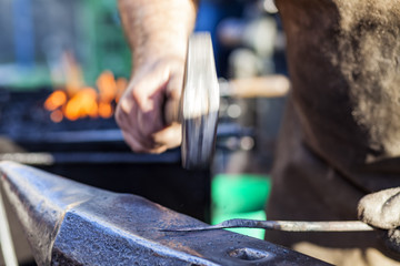 Blacksmith hammering iron rod on anvil in background fire