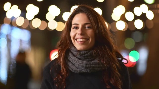 Attractive Caucasian young female in grey scarf and coat winking smiling laughing at camera in slowmotion