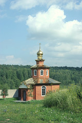 Fototapeta na wymiar Bricks orthodox chapel with dome amidst summer meadow