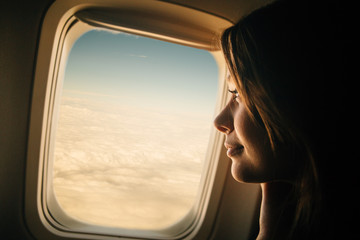 Young woman looking through window in airplane - obrazy, fototapety, plakaty