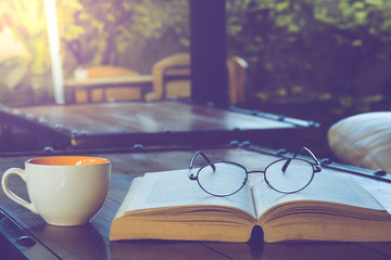 A cup of black coffee with reading glasses on table and open book in cafe