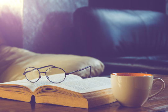 A Cup Of Black Coffee With Reading Glasses On Table And Open Book In Cafe