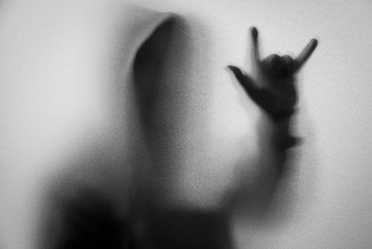 Shadow blur of horror man in jacket with hood.Hands do as a symbol love on the glass.Dangerous man behind the frosted glass.Mystery man.Halloween background.Black and white picture.Blur picture.