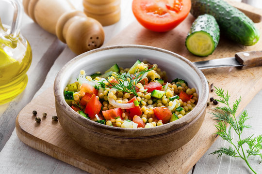 Traditional Israeli healthy meal Ptitim with tomatoes, cucumber and onion for delicious healthy breakfast. Cooking of classic Moroccan couscous with vegetables.