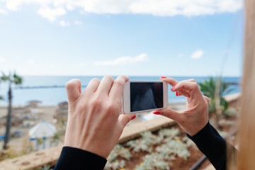 Woman photographing ocean and beach with her smartphone