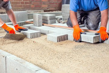 Hands of two builders laying paving stones.