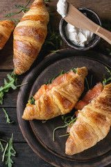 Croissant with smoked salted salmon, spinach and arugula served with bowl of cream cheese over dark old wooden background. Top view