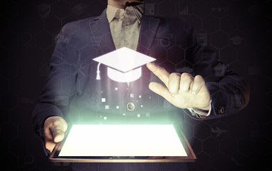 Image of a man with a tablet in his hands. He presses on the icon graduation hat cap. Online...