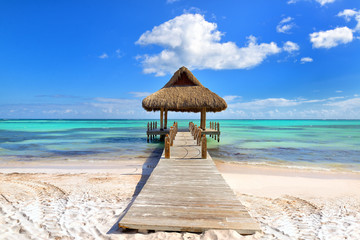 Tropical white sandy beach. Palm leaf roofed wooden pier with gazebo on the beach. Punta Cana, Dominican Republic