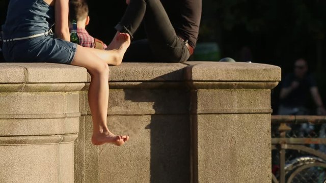 A pretty woman lets her legs dangling on a bridge in Berlin, the water reflects the sunset. A sip of beer were taken