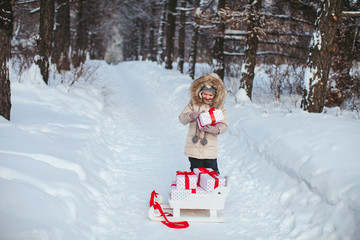 Fototapeta na wymiar little cheerful girl holding a box with a gift in a winter forest