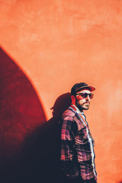 Bearded man in cap and sunglasses on red wall in sunlight