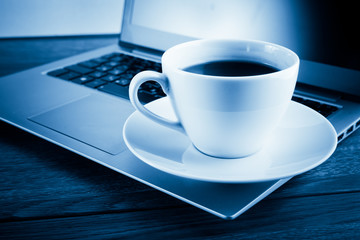 Cup of coffee and laptop on wooden table.