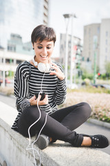 Young beautiful caucasian short brown hair woman with smart phone hand hold and headphones around...