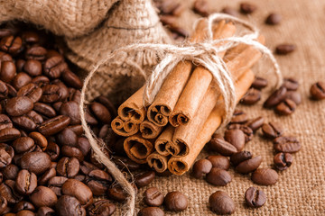 Coffee beans and cinnamon on a background of burlap. Roasted coffee beans background close up. Coffee beans pile from top with copy space for text. Seasoning. Spice. Cinnamon. Badian. Coffee house.