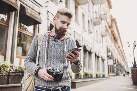 Outdoor portrait of modern young traveler man using smart phone on the street