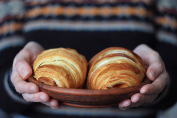  woman's hands holding a plate of croissants, selective focus, background sweater with a jacquard pattern, close-up