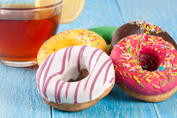 pile of glazed donuts with a cup of tea on a blue wooden background