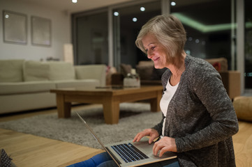 Senior woman sitting on the floor working on laptop