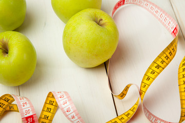 Green apples with measuring tape on a white wooden table