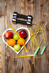 White heart, apples and oranges, healthy diet, dumbbells  a jump rope on  wooden background
