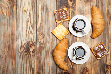 Two cups of coffee, croissant, toast and chocolate on wooden table
