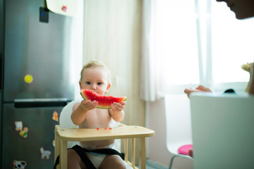 Cute little girl sitting in high chair eating watermelon