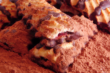 Pile of shortbread cookies with jam and chocolate icing on the scattered cocoa powder