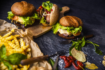 Fast food on the table: hot dog sausage and vegetables, burger with pork or beef and French fries with tomato sauce, basil leaves