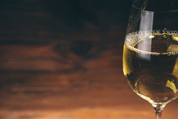 Pouring white wine from a bottle in a close up view of the wineglasses against wooden background