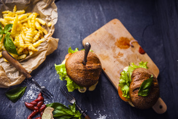 Fast food on the table: burger with beef or pork, or chicken and vegetables, French fries with tomato sauce, basil leaves