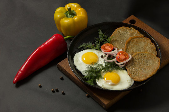 Fried eggs with potato pancakes and herbs in a pan on a black background. Homemade food.