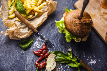 Fast food on the table: burger with beef or pork, or chicken and vegetables, French fries with tomato sauce, basil leaves