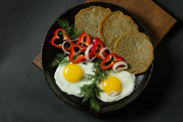 Fried eggs with potato pancakes and herbs in a pan on a black background. Homemade food.