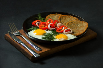Fried eggs with potato pancakes and herbs in a pan on a black background. Homemade food.