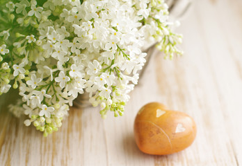 Fototapeta na wymiar Bouquet of a white lilac in a basket and heart with stones on a wooden surface, soft focus. Spring romantic bouquet. Greeting card for lovers, friendship or valentine's day.