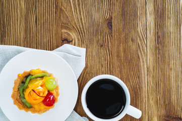 Appetizing cake basket with sliced fruit, berries and cup of coffee, on rustic wooden background with copy space. Delicious and fresh dessert and coffee, top view, flat lay.  Morning choice.