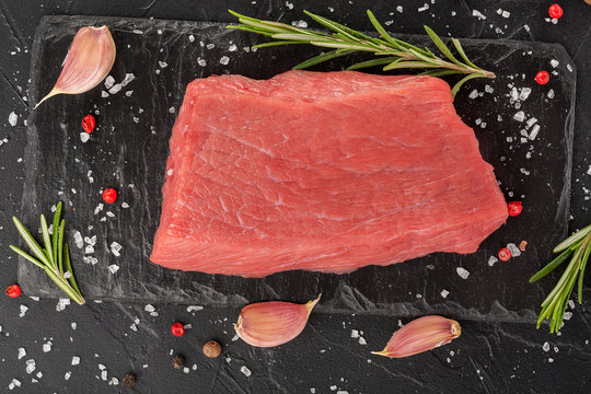 Steaks raw meat with spices on black stone background