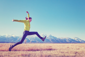 Color toned image of happy young woman jumping on a meadow, Grand Teton mountain range in distance, Wyoming, USA.