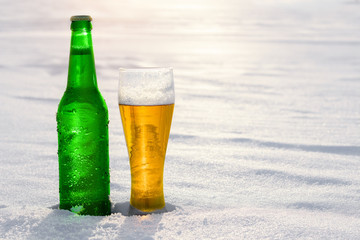 Mug and bottle of cold beer in the snow at sunset. Beautiful winter background. Outdoor recreation....
