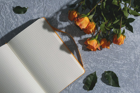 Opened yellow blank notebook and a bouquet of yellow roses on a blue table on a sunny morning. Top view.