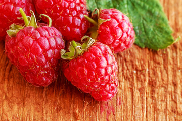 Rustic fresh ripe raspberries with leaves on brown background. Copy space. Close up. Front view.