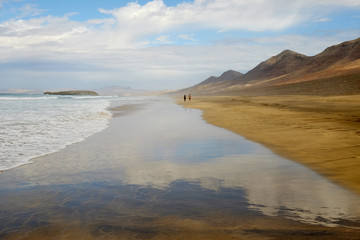 Fototapeta na wymiar View on the beach Cofete with two unknown walking persons far away on Fuerteventura, Spain.