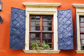 Old wooden vintage square window with open metal shutters on background of orange wall of house
