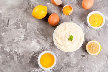 Mayonnaise with ingredients for cooking - eggs, vegetable oil, mustard, lemon, parsley. On the grey stone concrete table top view copy space