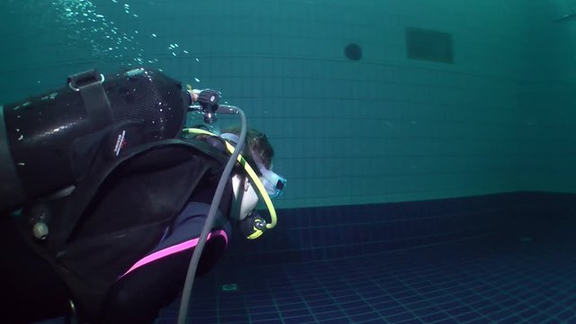 Two girls diver in a dive gear swimming using only one scuba gear for breathing.
