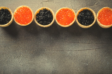 Black and red caviar tartlets, appetizer canapes on gray background, top view