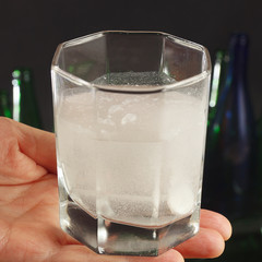 Hand with a glass of water and soluble pill of a hangover on a dark background.