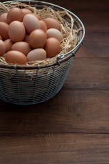Fresh Farm Chicken Eggs in Rustic Metal Wire Basket with Raffia on a Brown Wooden Farm Table Vertical with Copy Space